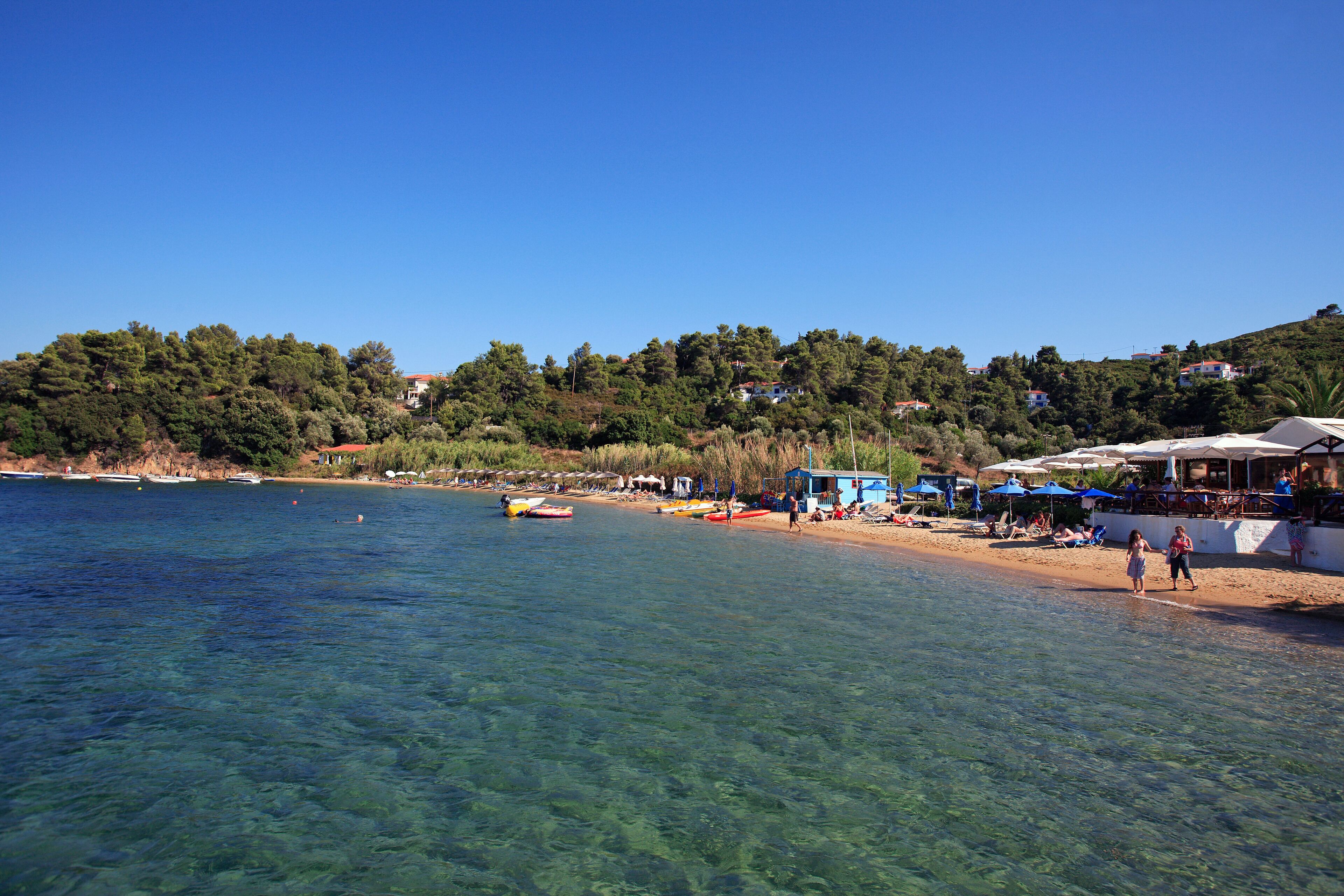 A clear coastal area with boats, a sandy beach, and buildings on a hillside.