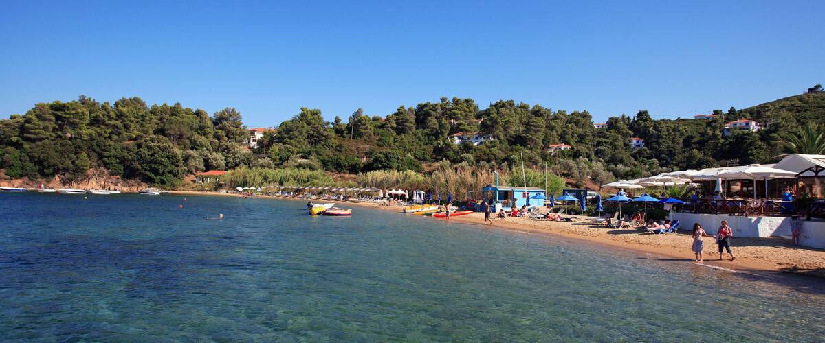 A clear coastal area with boats, a sandy beach, and buildings on a hillside.
