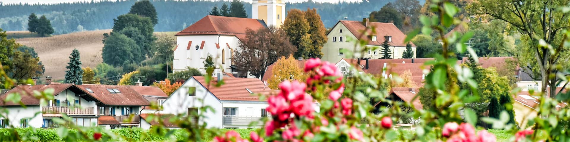 A village with a prominent church tower, surrounded by houses and lush greenery.