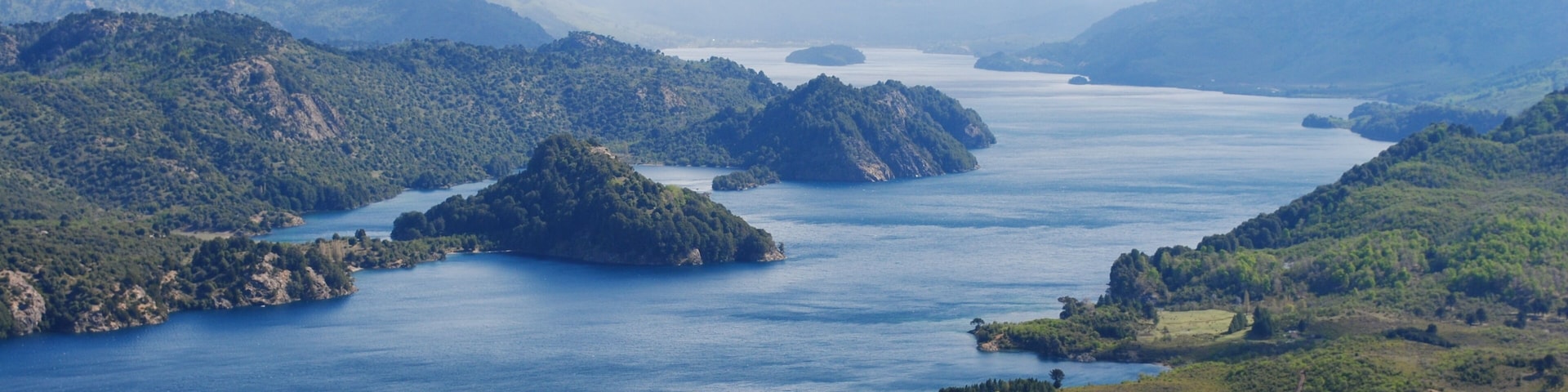 Un paisaje montañoso con un lago extenso rodeado de colinas y un pequeño pueblo.