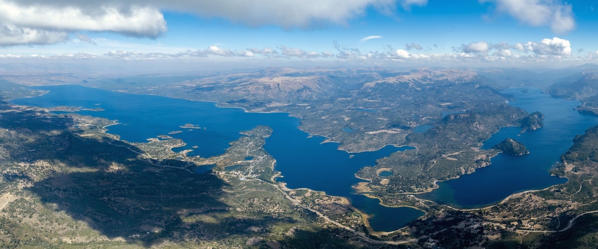 A vast aerial view of a coastal region with multiple inlets and peninsulas surrounded by dense forests and rugged terrain.