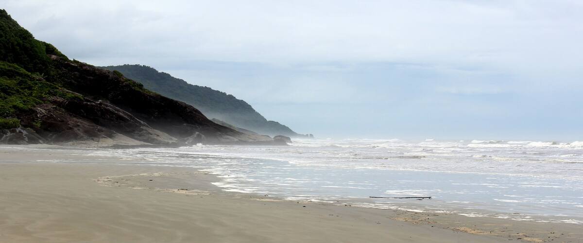A beach with a sandy shore, waves crashing onto the beach, and a hill with greenery in the background.