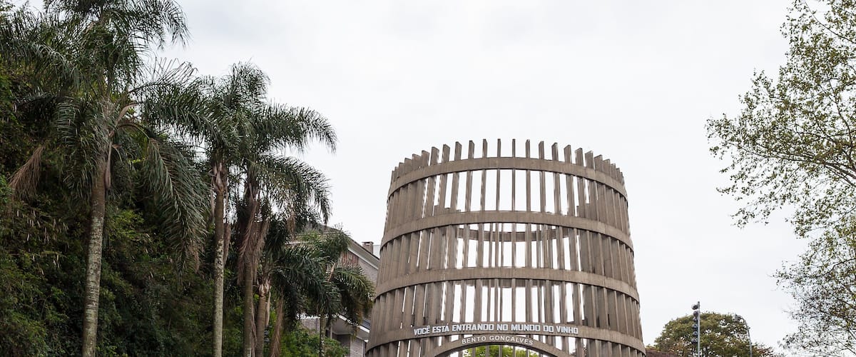Un arco de madera con un cartel que dice 'Bento Goncalves' y un camino que atraviesa un área verde con árboles.