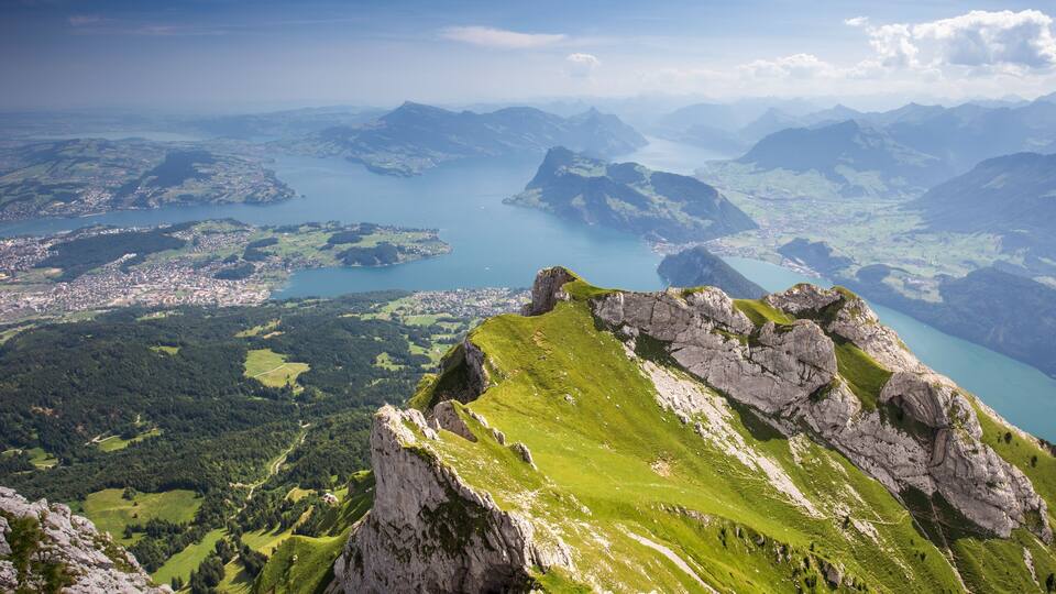 A mountainous landscape with a lake, green valleys, and rocky peaks.
