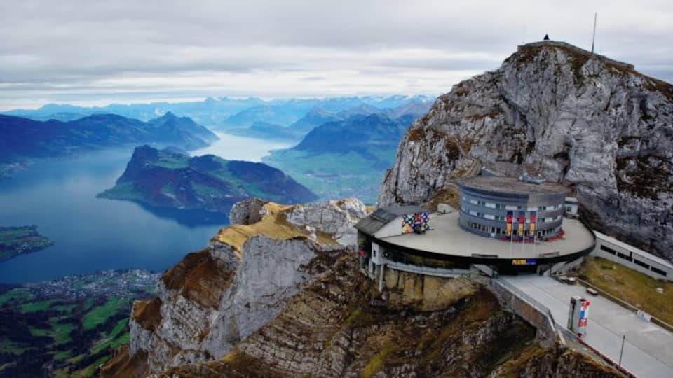 A mountain lodge with a circular building overlooking a fjord and mountains.