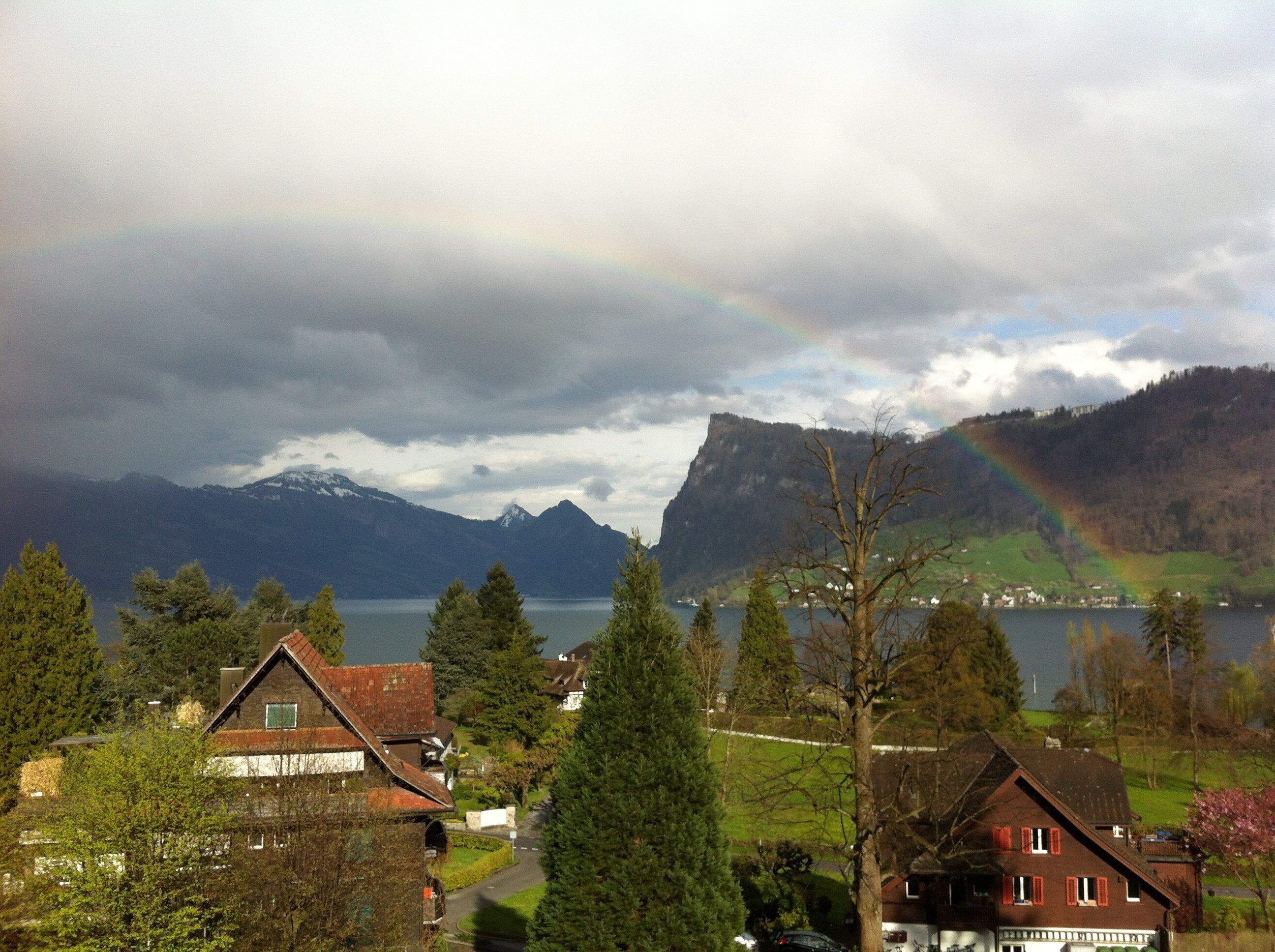 A mountain landscape with a lake, houses, and a rainbow.