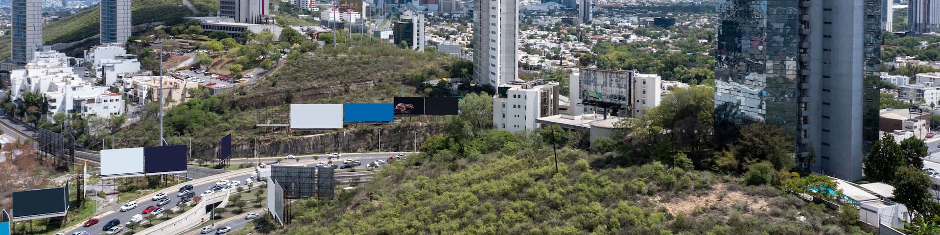 A cityscape with modern skyscrapers, a highway, and mountains in the background.