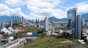 A cityscape with modern skyscrapers, a highway, and mountains in the background.