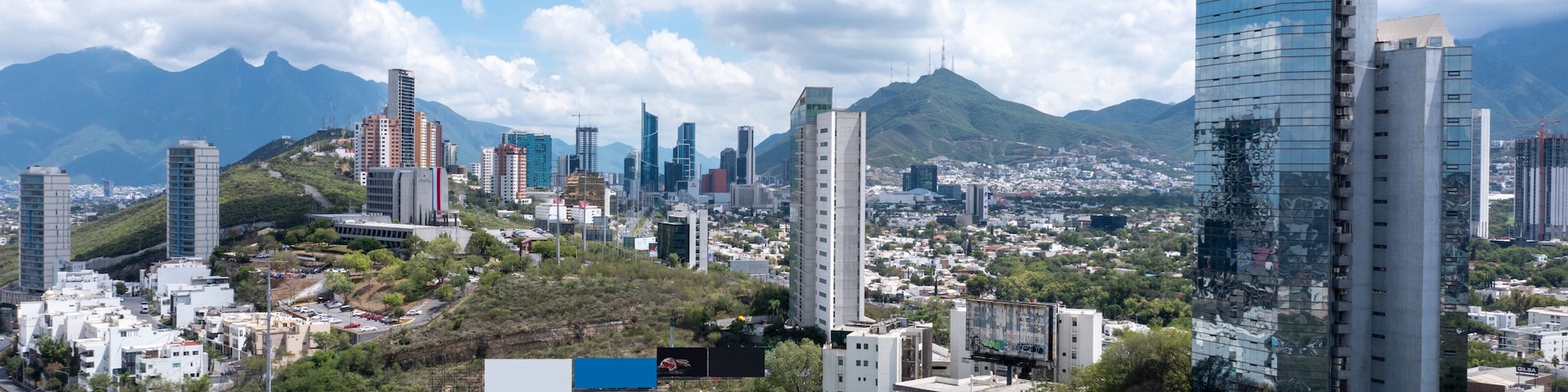 Une vue urbaine avec des gratte-ciel modernes, une autoroute et des montagnes en arrière-plan.