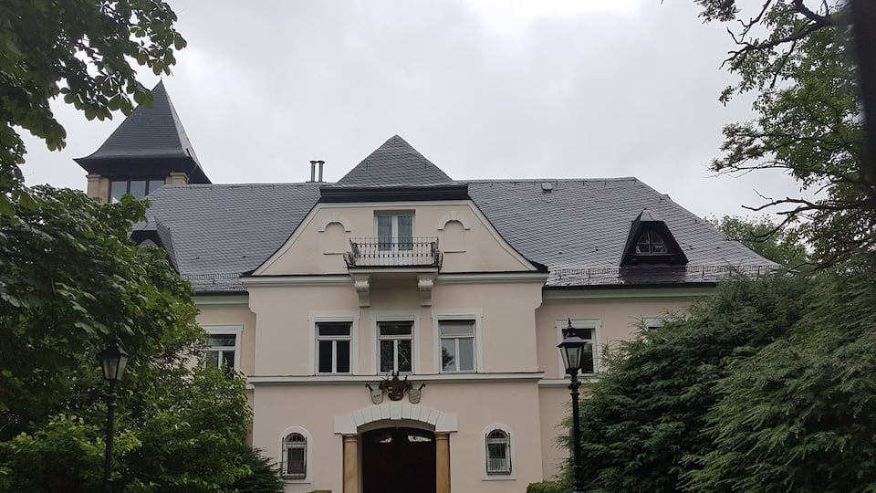 A large, stately building with a steep roof, a balcony, and a gated entrance.