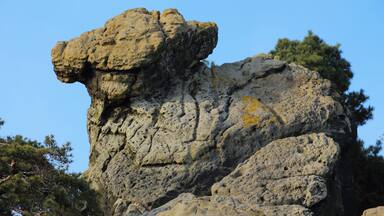 A large rock formation with a prominent overhang against a clear blue sky.