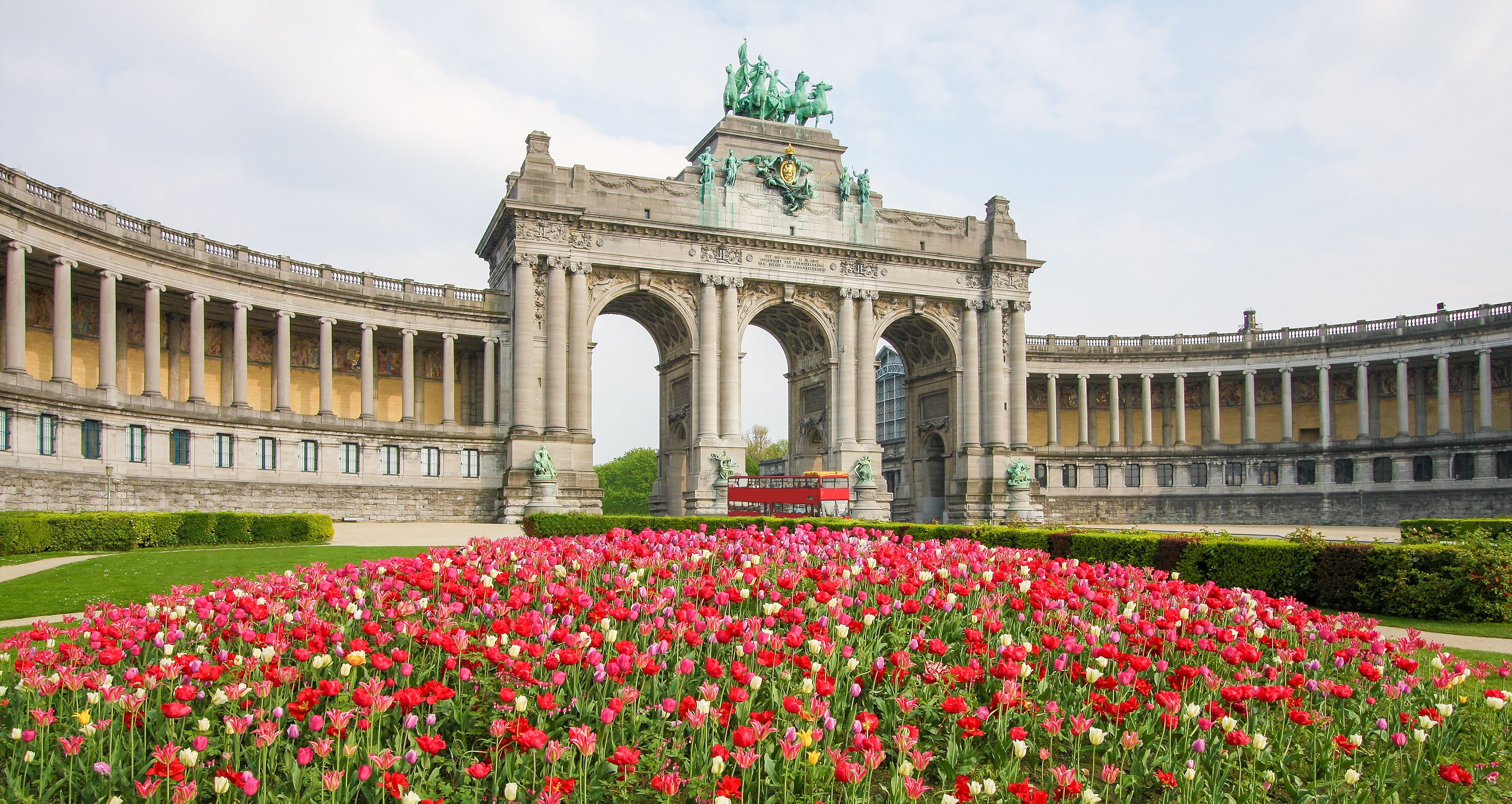 Un imposant bâtiment doté d’une arche centrale, avec un champ de tulipes aux couleurs vives en premier plan.