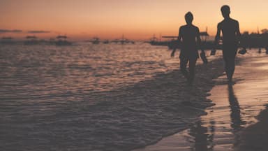 Traditional philippine boats floating in the sea and silhouettes of a woman and man walking along the sea shore during sunset. Panglao Island, Philippines.