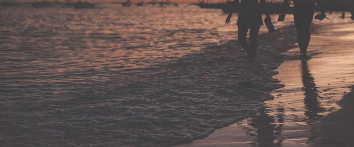 Traditional philippine boats floating in the sea and silhouettes of a woman and man walking along the sea shore during sunset. Panglao Island, Philippines.