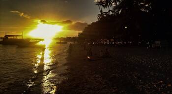 A sunset over a beach with palm trees and boats.