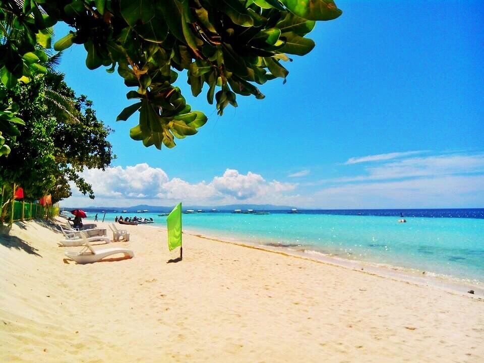 A beach with clear turquoise water, white sand, and a few people in the distance.
