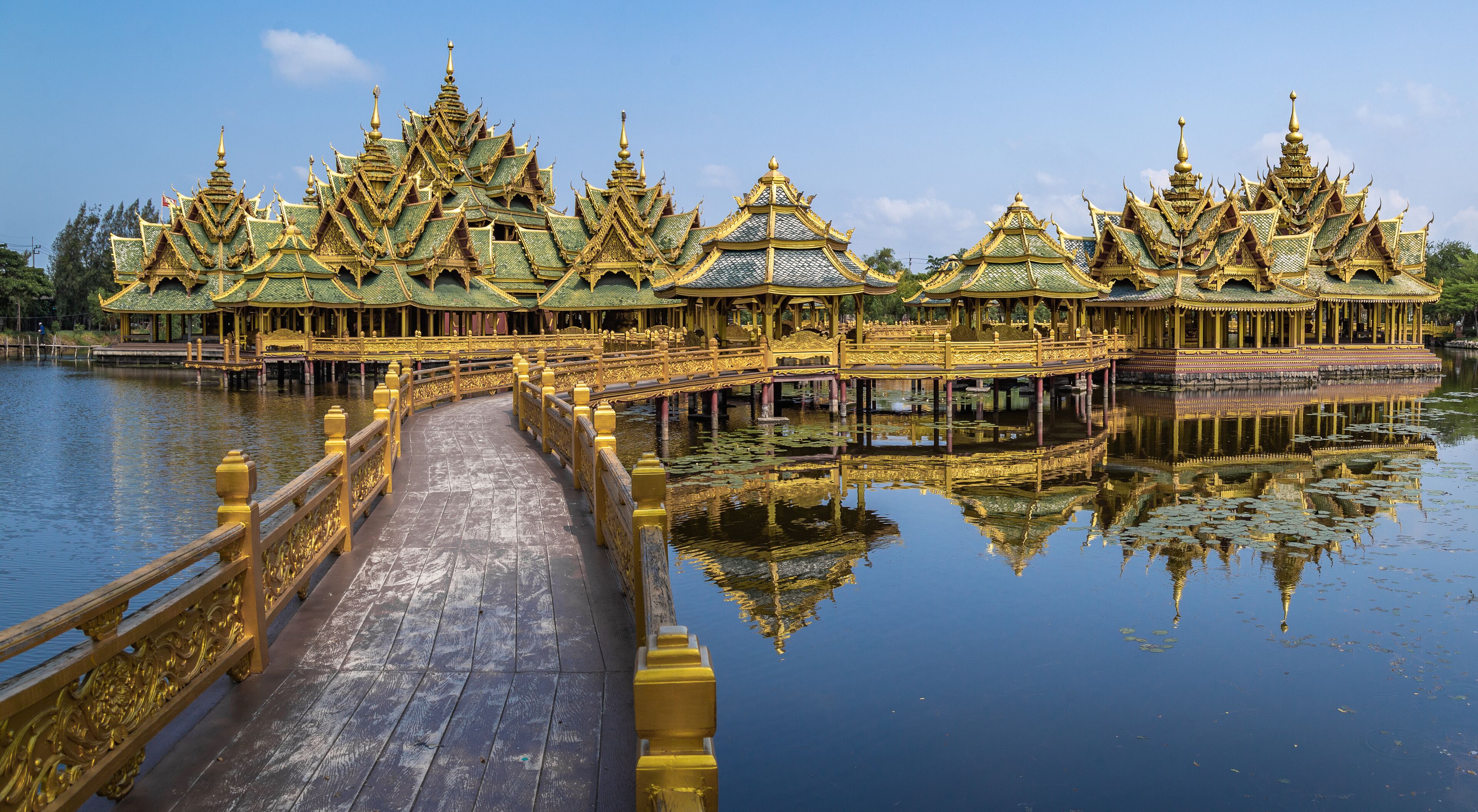 A golden temple complex with ornate roofs and a wooden bridge over water.
