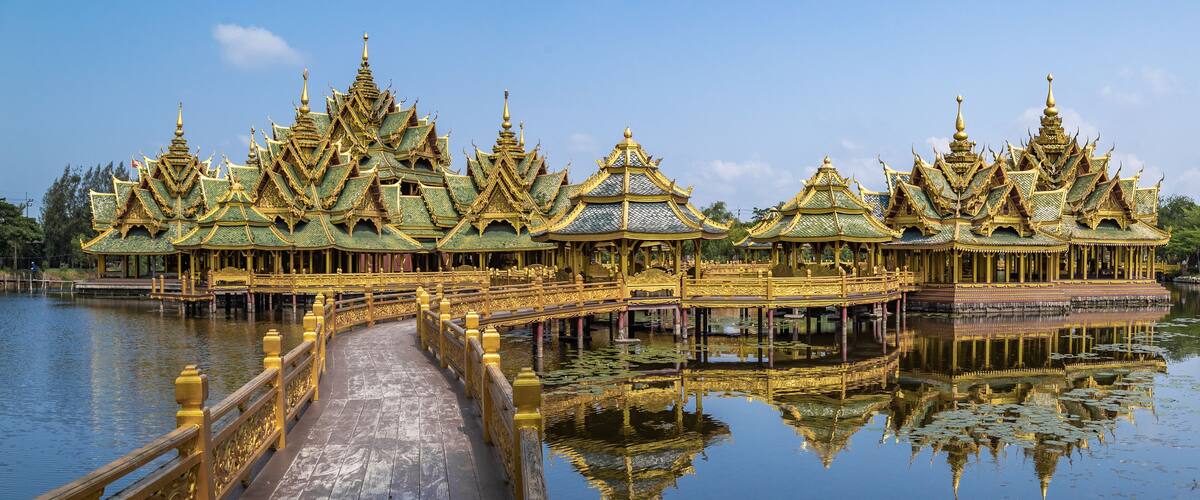 A golden temple complex with ornate roofs and a wooden bridge over water.