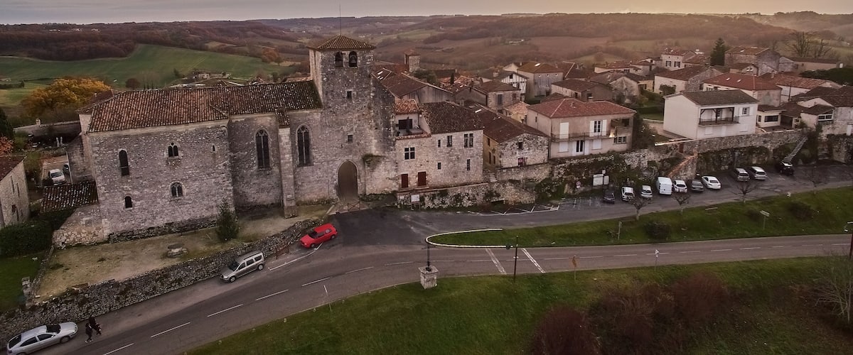 An aerial view of a historic town with a prominent church, a winding road, and surrounding countryside.