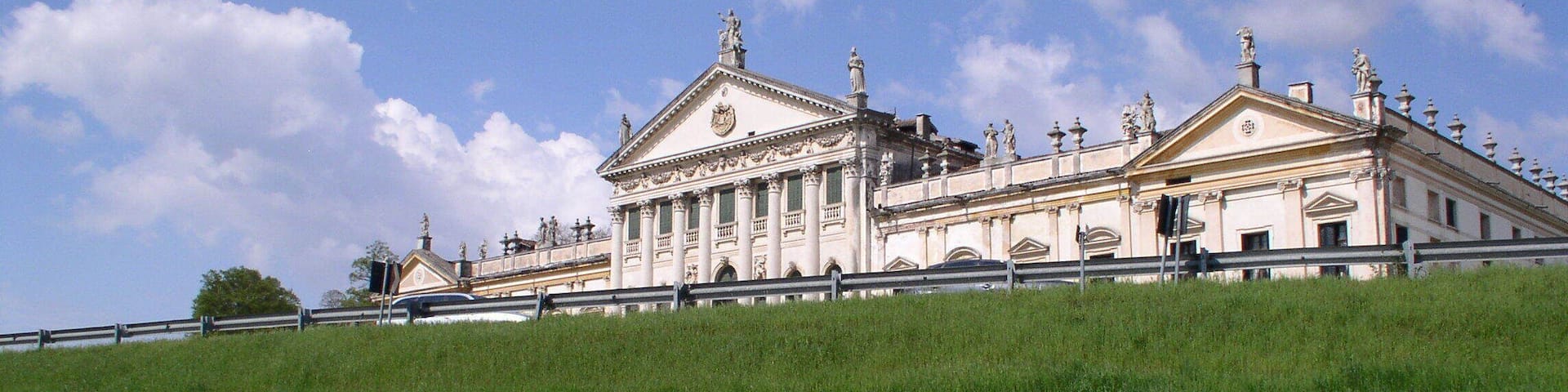 A classical building with columns and statues, located beside a body of water.