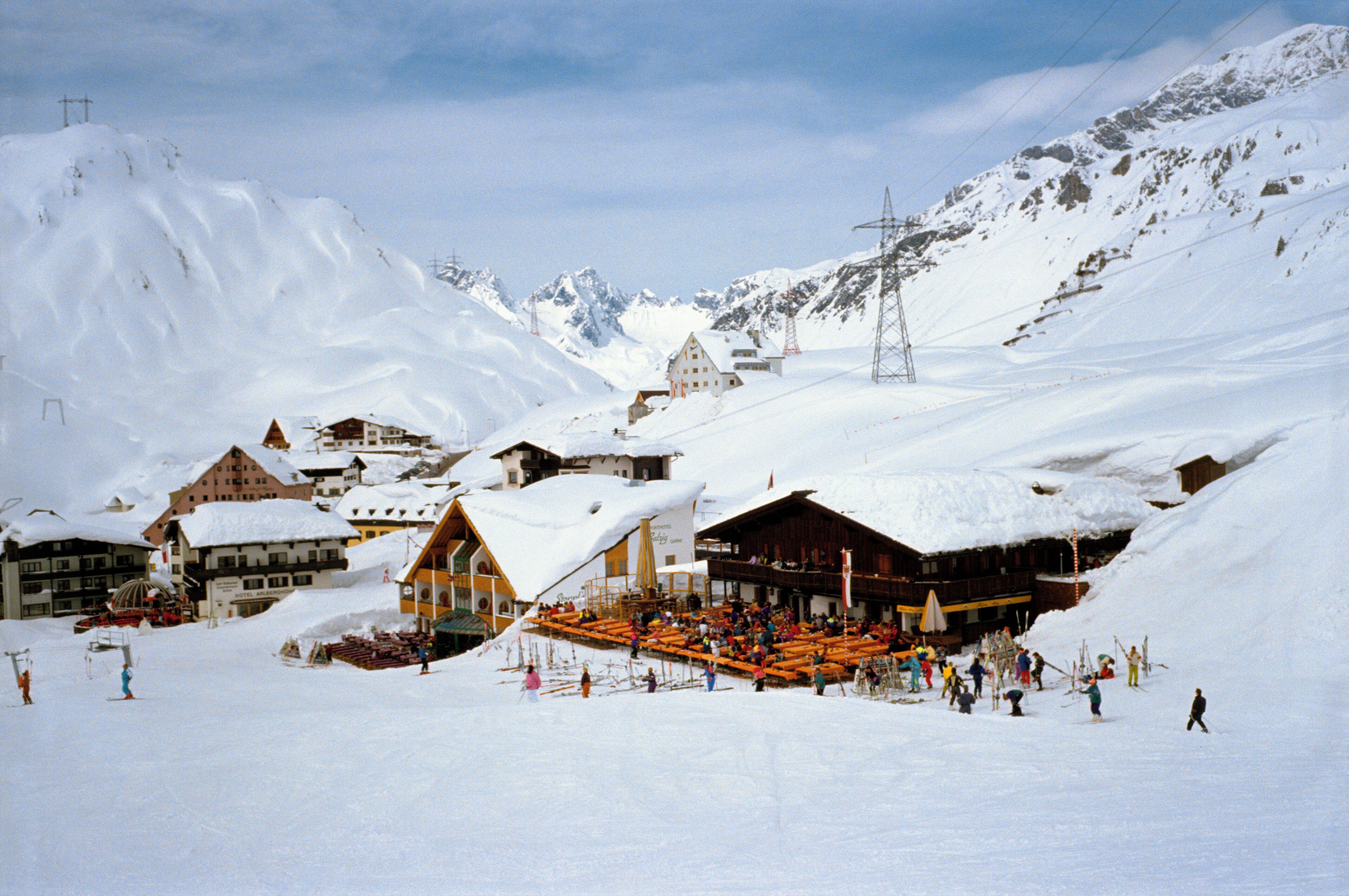 A snow-covered ski resort with buildings, a ski lift, and a mountainous backdrop.