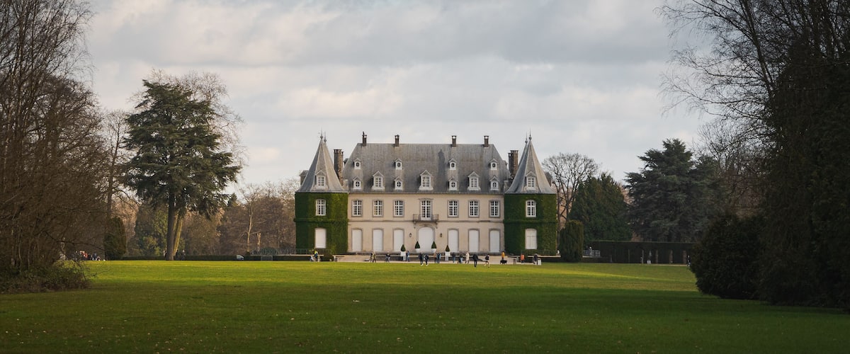 A large, historic building with a green facade and multiple windows, surrounded by a well-maintained lawn and trees.