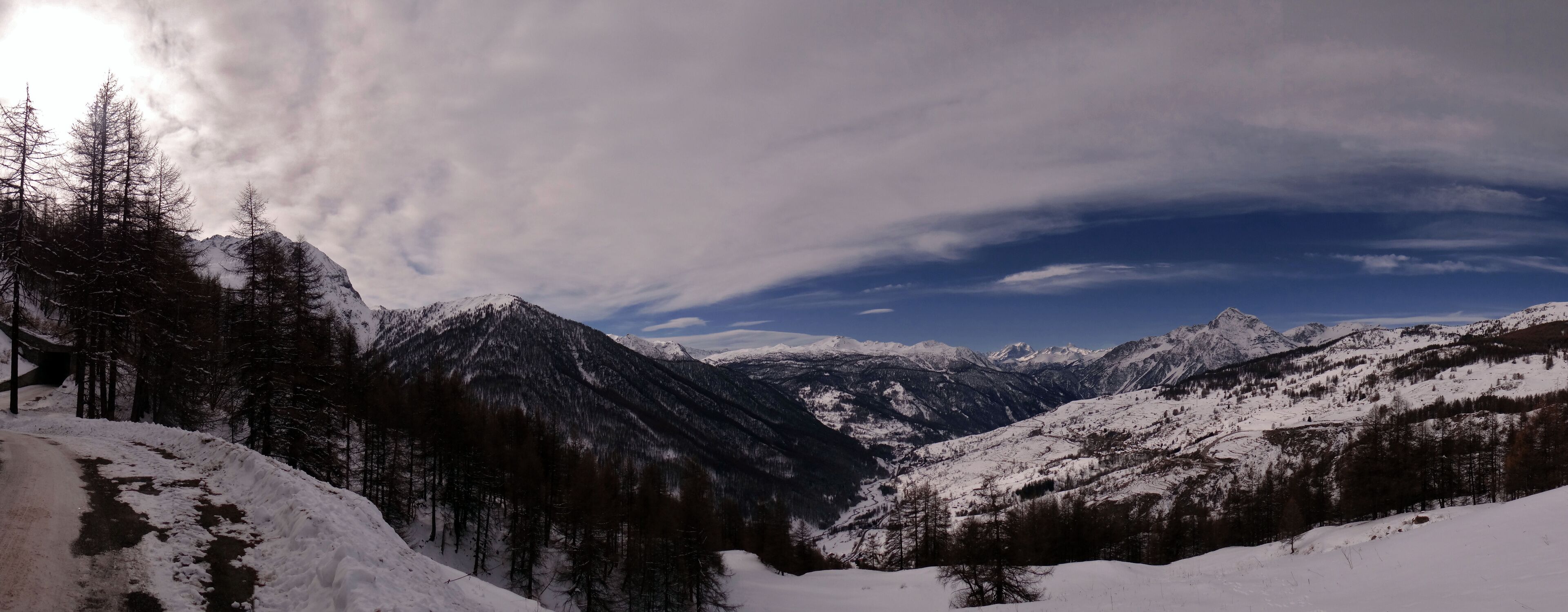 A snow-covered mountain range with a winding road and dense forest.