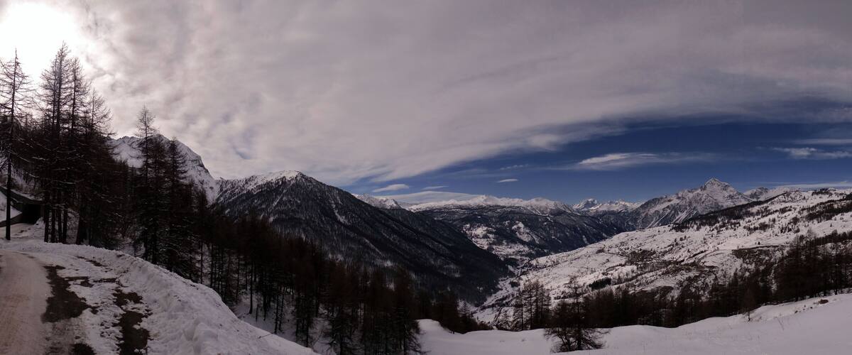 A snow-covered mountain range with a winding road and dense forest.