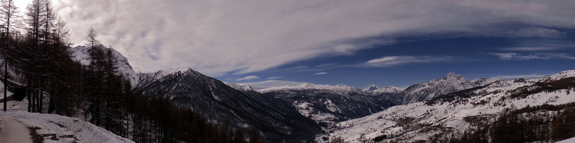 A snow-covered mountain range with a winding road and dense forest.