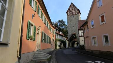 A narrow street with historic buildings, a tower, and a stone archway.