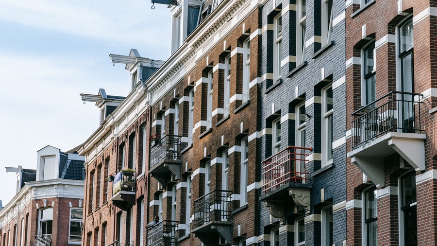 Une rangée d’immeubles en briques rouges, avec des ornements blancs et des balustrades noires sur les balcons.
