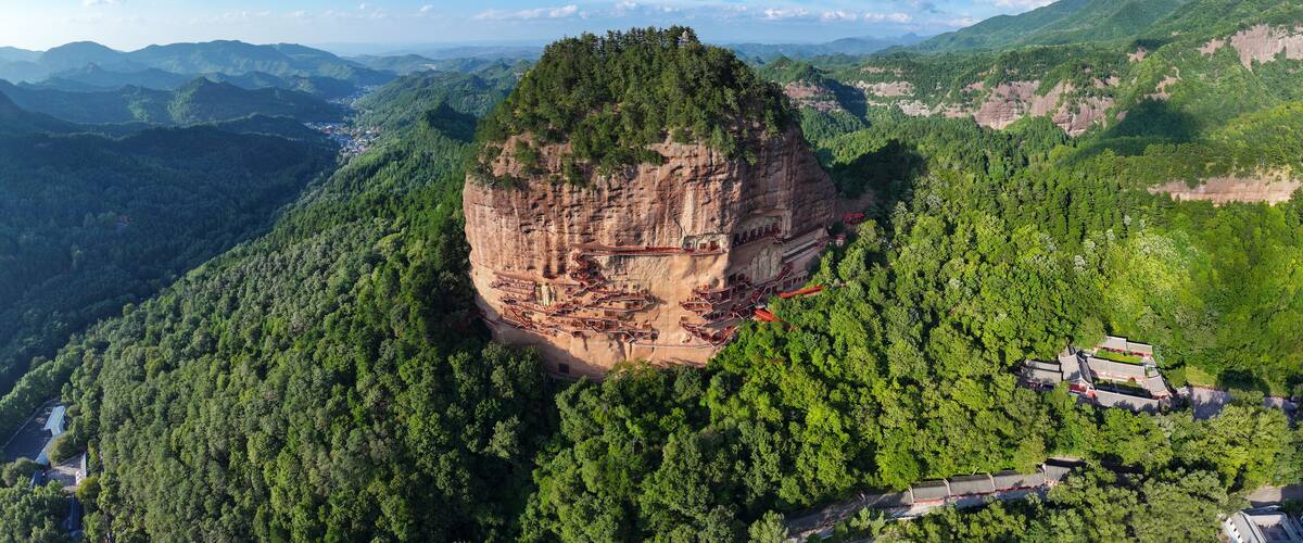 A cliffside monastery with a steep, forested mountain backdrop.