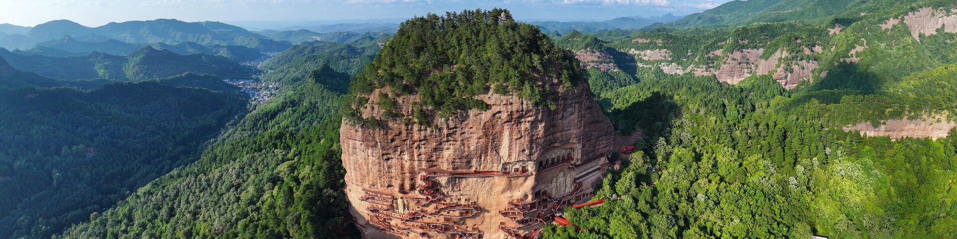 A cliffside monastery with a steep, forested mountain backdrop.