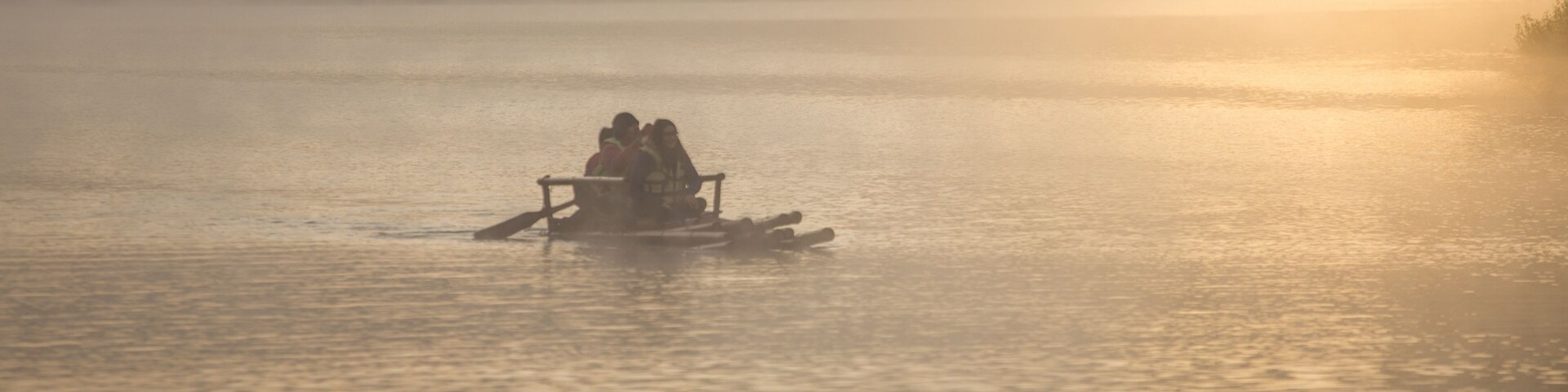 Un lago tranquilo con un bote llevando gente, rodeado por un bosque brumoso.