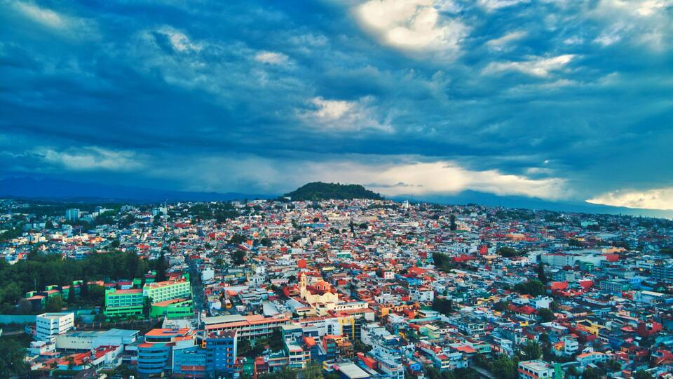A densely populated cityscape with colorful buildings under a cloudy sky.