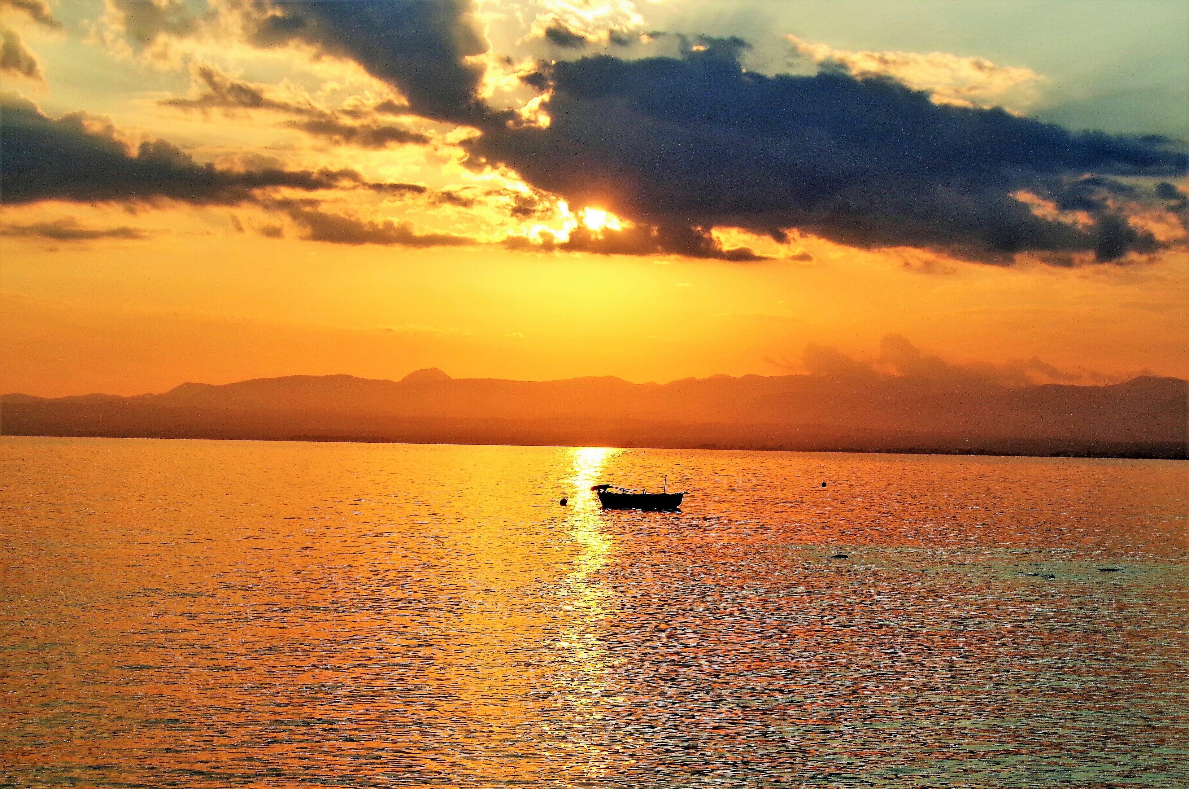A boat on a calm body of water during sunset with a mountain range in the background.