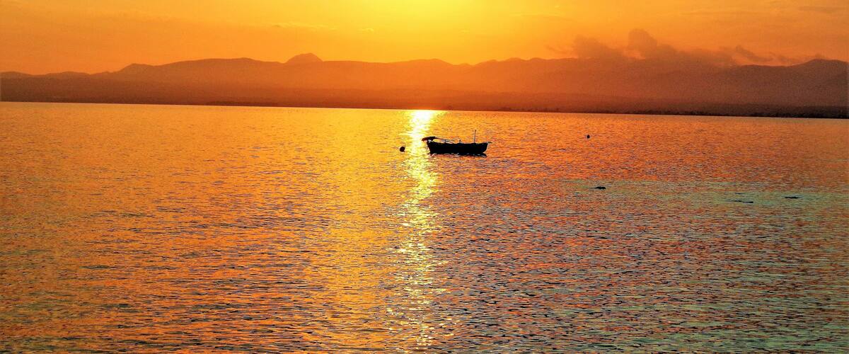 A boat on a calm body of water during sunset with a mountain range in the background.