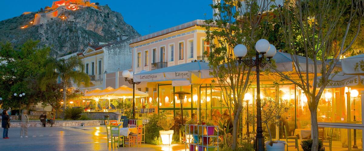 A waterfront promenade with outdoor cafes, a mountain in the background, and a historic fort.