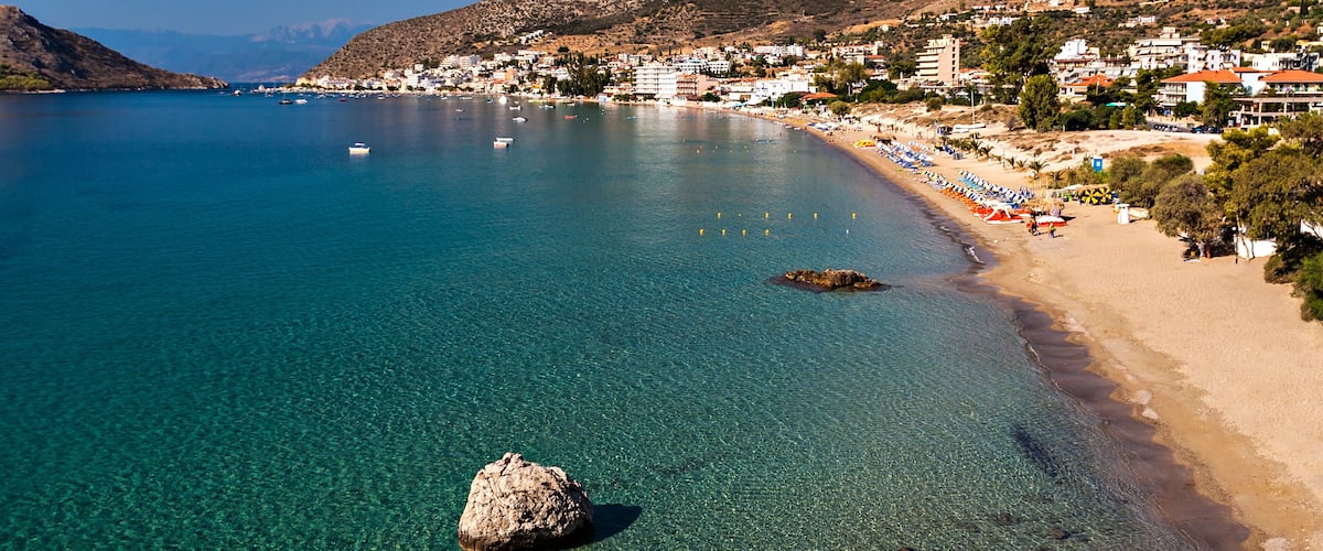 A coastal town with clear blue waters, a sandy beach, and buildings along the shore.
