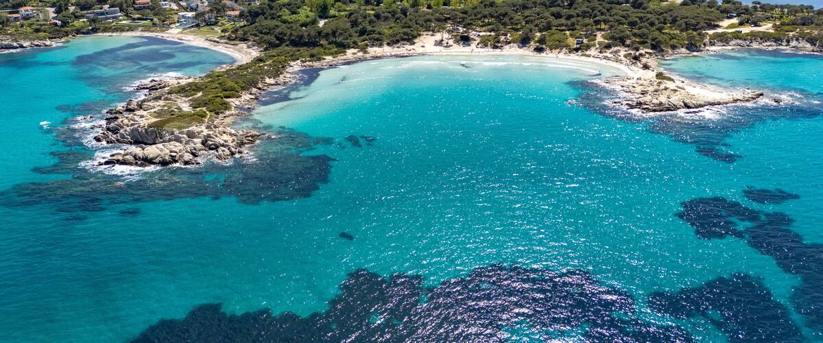 A coastal landscape with clear turquoise waters, rocky outcrops, and a dense forested area.