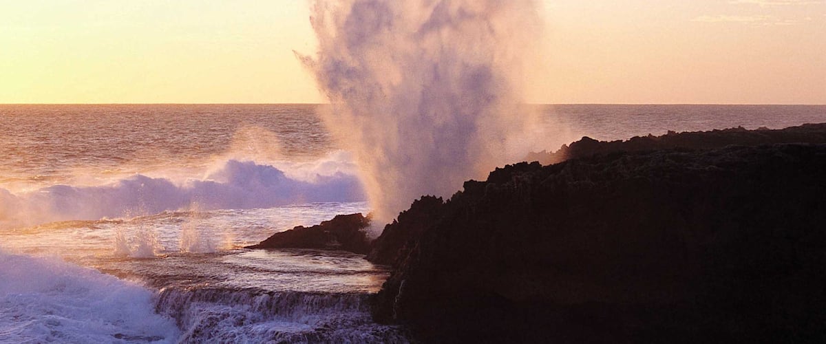 A coastal scene with waves crashing against a rocky shore at sunset.