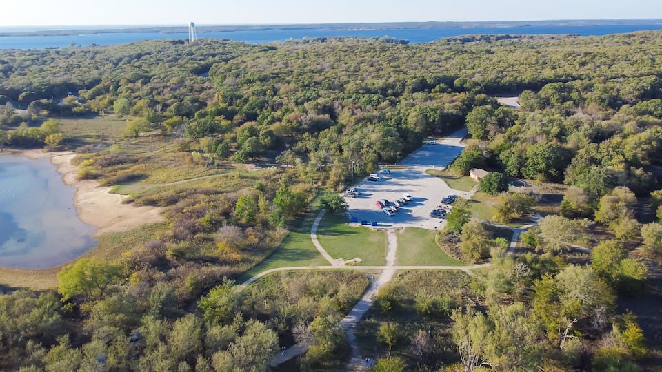 An aerial view of a coastal area with a parking lot, a walking path, and dense vegetation.