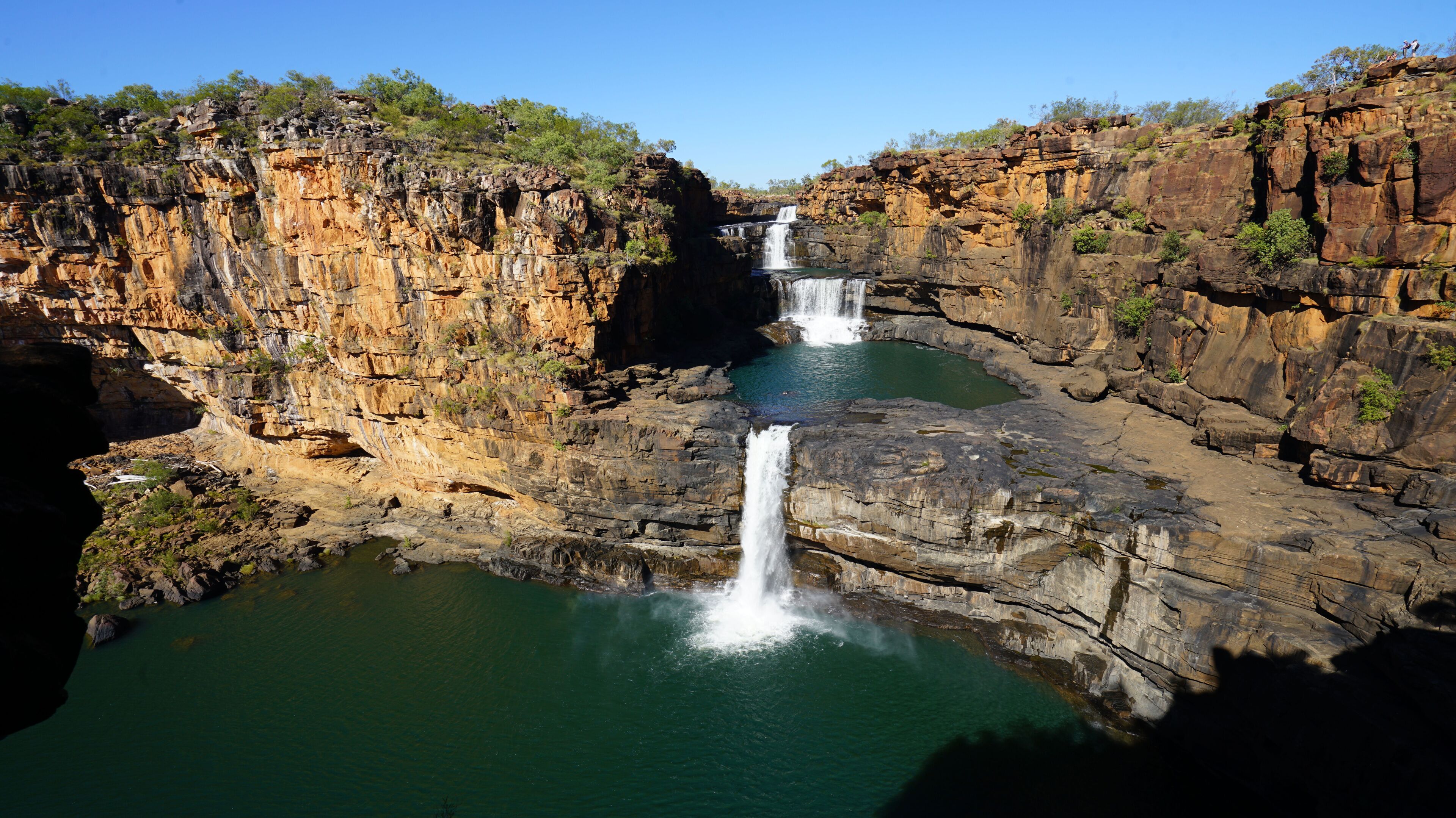 A multi-tiered waterfall cascading into a clear pool surrounded by rugged cliffs.