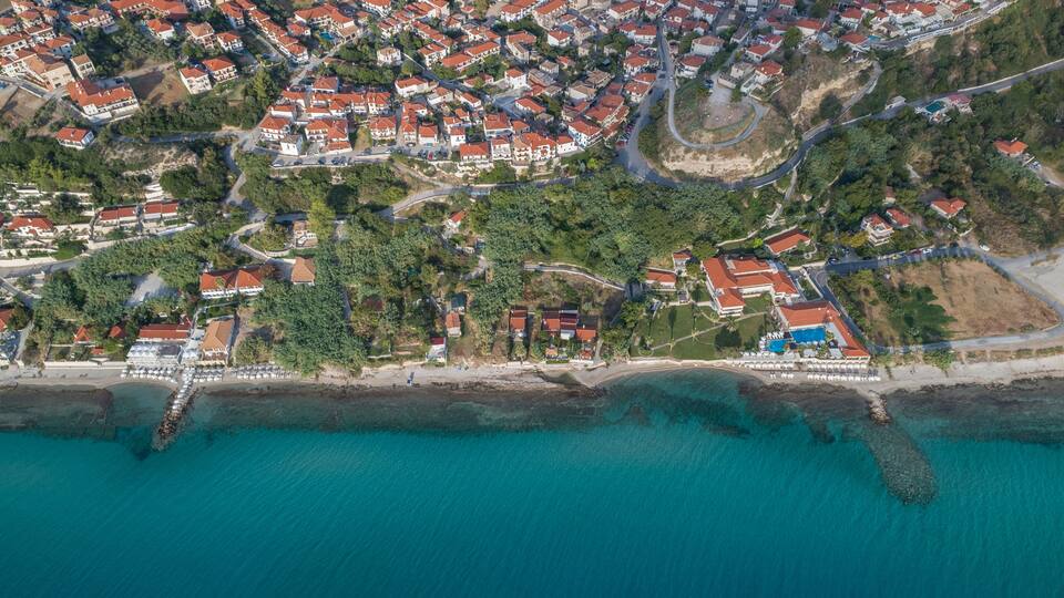 An aerial view of a coastal town with red-roofed houses, a beach, and clear turquoise waters.