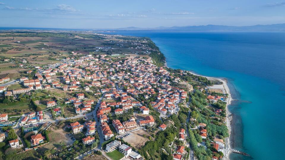 An aerial view of a coastal town with red-roofed houses, a beach, and a clear blue sea.