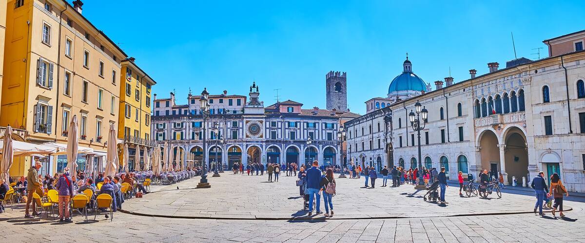 A historic square with cobblestone pavement, a prominent clock tower, and classical architecture.