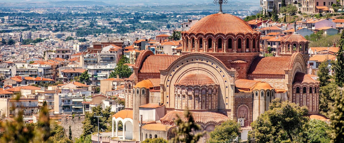 A cityscape with a prominent church featuring a red-tiled dome and arched windows, surrounded by residential buildings and mountains in the background.