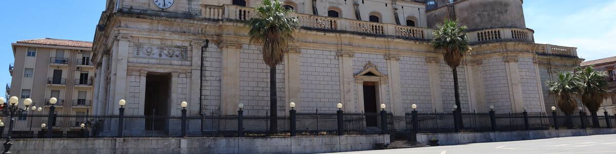 A historic building with a clock tower, a dome, and palm trees in front.