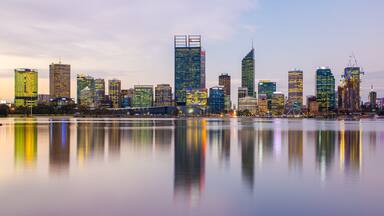 A city skyline with modern skyscrapers and a calm body of water reflecting the buildings.