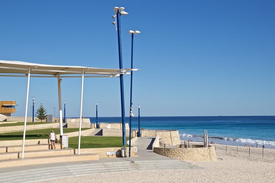 Platja amb una zona d'estar coberta, una paret de pedra i un cel blau clar.